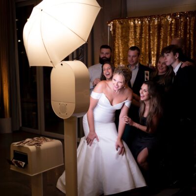 Bride and guests enjoying a photo booth experience at a Mississauga wedding with gold backdrop and instant prints.