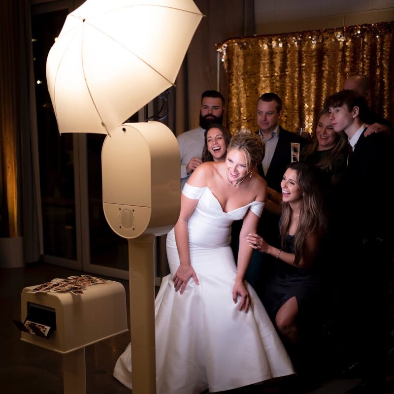 Bride and guests enjoying a photo booth experience at a Mississauga wedding with gold backdrop and instant prints.